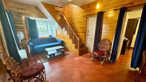 Een gezellige woonkamer met een blauwe bank, houten vloeren, een trap en rieten stoelen.