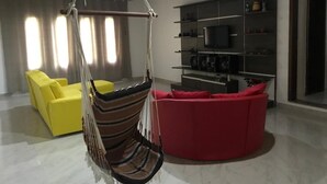 Ein Wohnzimmer mit Hängekorbsessel, einem roten Sofa, einem gelben Sofa und einem Fernseher auf einem Regal.