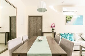A dining area with a wooden table, cushioned chairs, a hanging light fixture, and a wall-mounted air conditioner. - Paseo Del Mar B3A_200Mbps_Pool_Walk to Beach & Dining! (Bavaro-Punta Cana)
