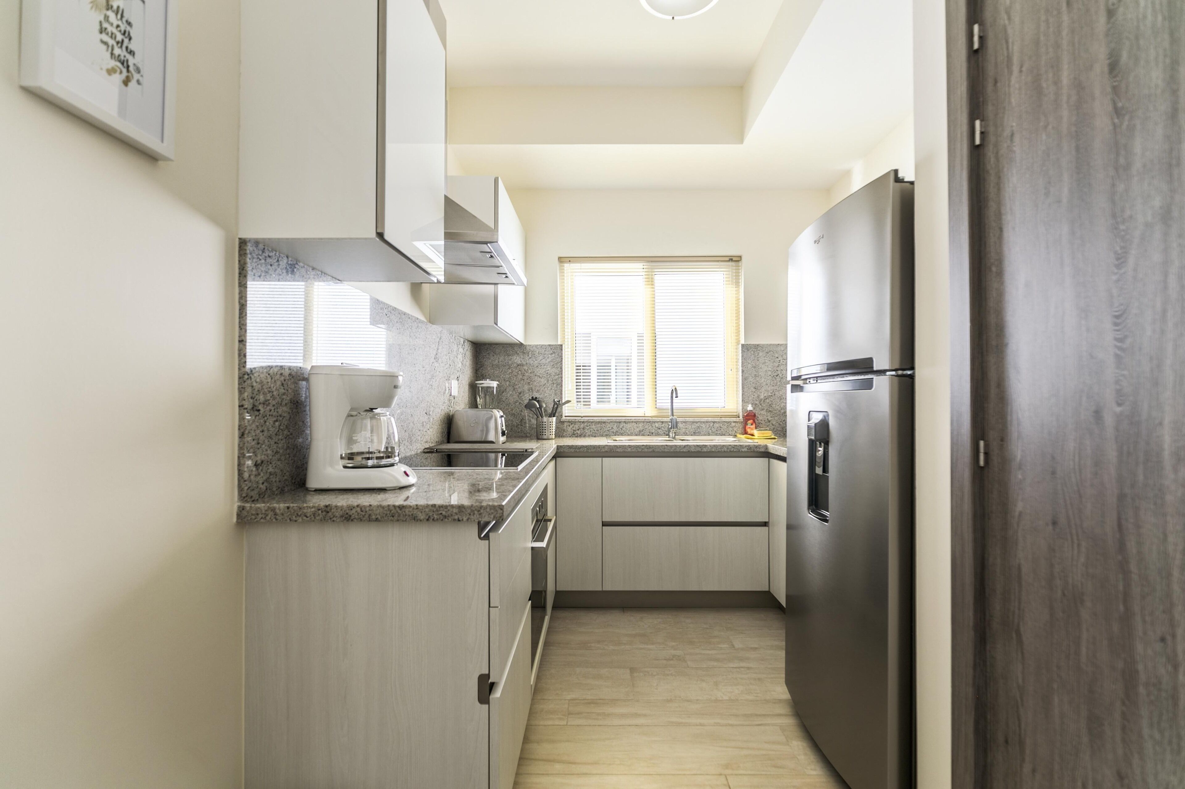 Een moderne keuken met granieten aanrechtbladen, roestvrijstalen apparatuur en lichte houten keukenkastjes.