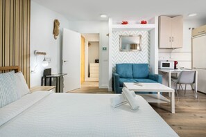 A modern hotel room with a large bed, a sofa, a small table, a desk, and a kitchenette.
