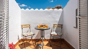 Een klein buiten terras met een tafel en twee stoelen, een witte muur en een helderblauwe lucht.