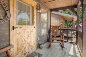 A wooden porch with a wooden door, a chair, and a table. - Double U Cowboy | 1BR Cabin with BBQ & Paddle Boat (Bandera)