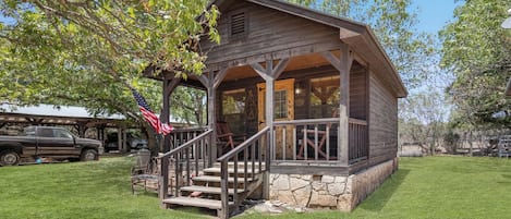 A rustic cabin with a porch, steps, and a flag.