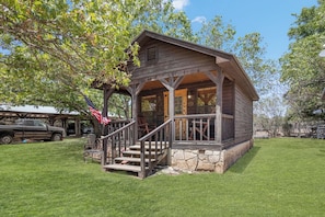 A rustic cabin with a porch, steps, and a flag. - Double U Cowboy | 1BR Cabin with BBQ & Paddle Boat (Bandera)