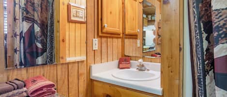 Un baño de madera con lavamanos, espejo y toallero.