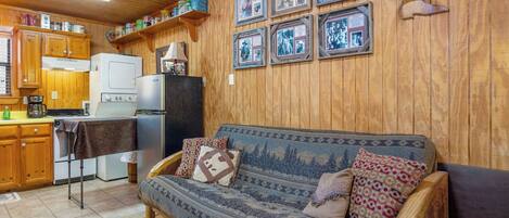 A cozy cabin interior with a wooden interior, a sofa, a dining table, and a refrigerator.