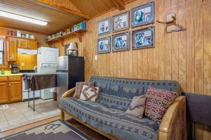 Un interior acogedor de cabaña con detalles de madera, un sofá, una mesa de comedor y un refrigerador.