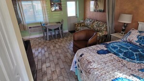 A bedroom with a bed, a chair, a table, and a painting on the wall. - Waterfront Ground Level Condo Only Steps From The Beach  (Englewood)