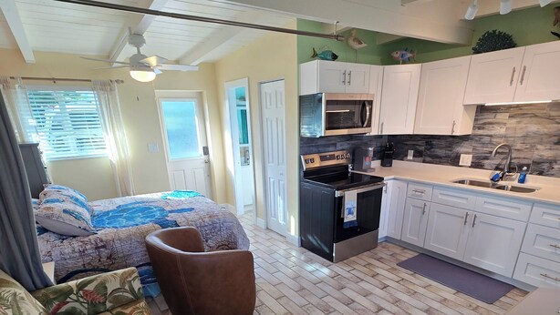 A compact living space with a sofa, a dining table, a kitchen area with white cabinets, and a ceiling fan. - Waterfront Ground Level Condo Only Steps From The Beach  (Englewood)