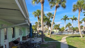 A covered patio with outdoor furniture, a grill, and a pathway lined with palm trees. - Waterfront Ground Level Condo Only Steps From The Beach  (Englewood)