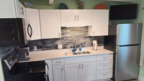 A kitchen with white cabinets, a stainless steel refrigerator, a black dishwasher, and a marble backsplash. - Waterfront Ground Level Condo Only Steps From The Beach  (Englewood)