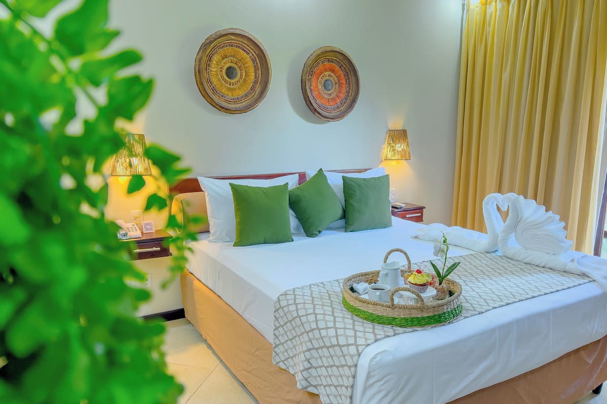 A neatly made bed with green pillows, a decorative swan, and a breakfast tray.