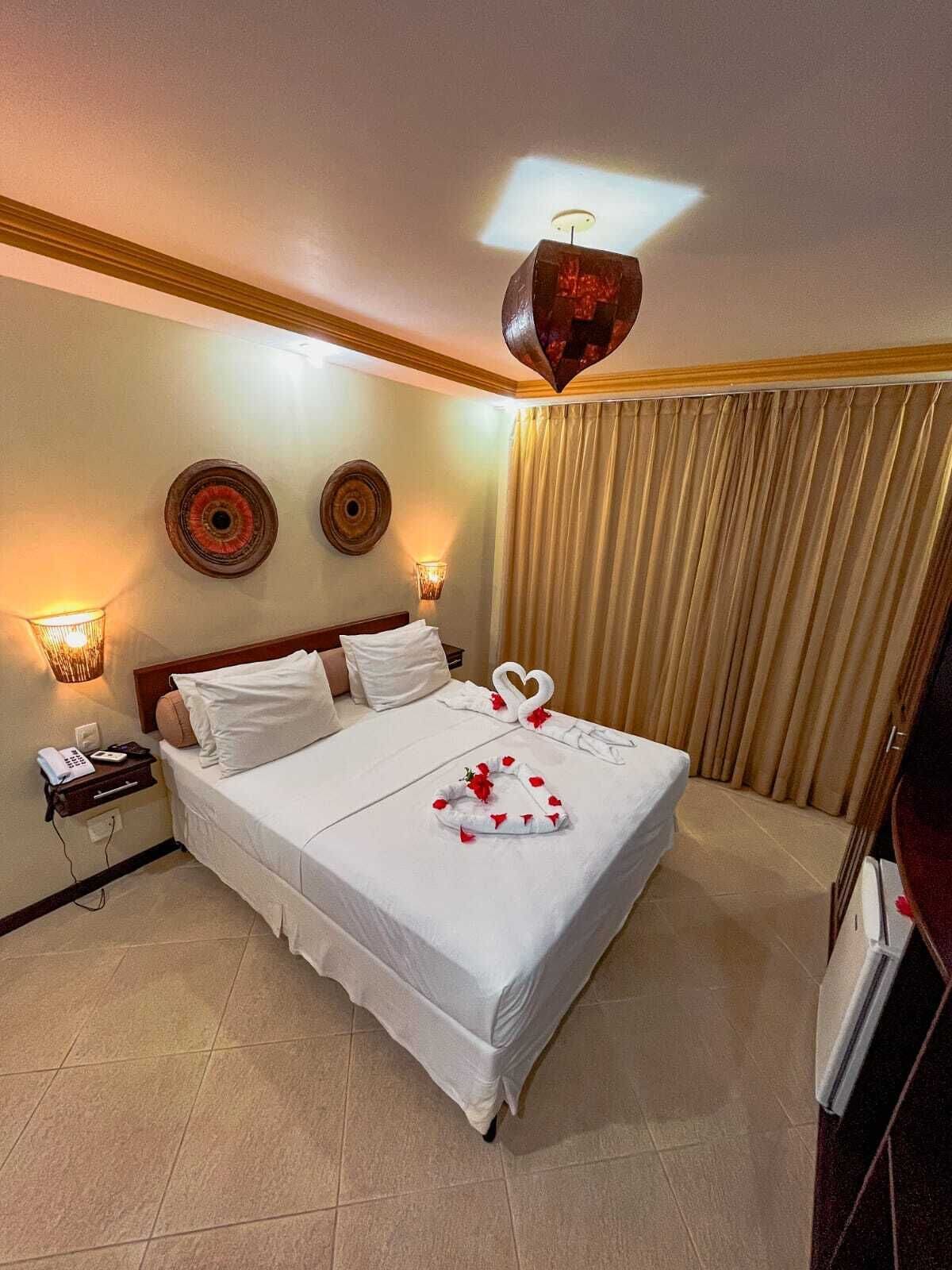 A hotel room with a large bed, two wall sconces, a telephone, and a decorative ceiling light.