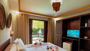 A hotel room with a large bed, a television, and a view of greenery outside. - Pousada Pérola do Porto (Ipojuca)