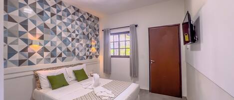Un dormitorio con cama, pared con estampado geométrico, ventana con cortinas, puerta y televisor montado en la pared.