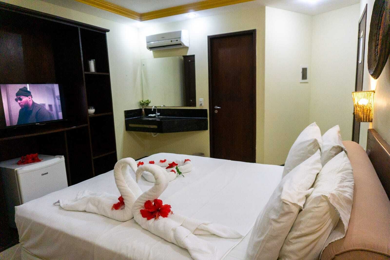 A hotel room with a bed, a television, a sink, and a mirror.