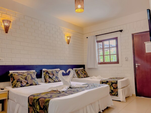 Habitación de hotel con pared de ladrillo blanco, dos camas con ropa de cama floral, una ventana con cortinas e iluminación empotrada.