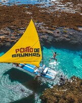 Una barca a vela con una vela gialla ancorata vicino a coste rocciose.
