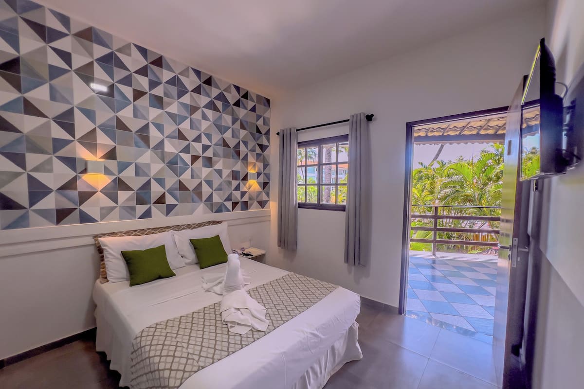 A hotel room with a geometric-patterned wall, a bed with white bedding and green pillows, a nightstand, and a window with curtains.