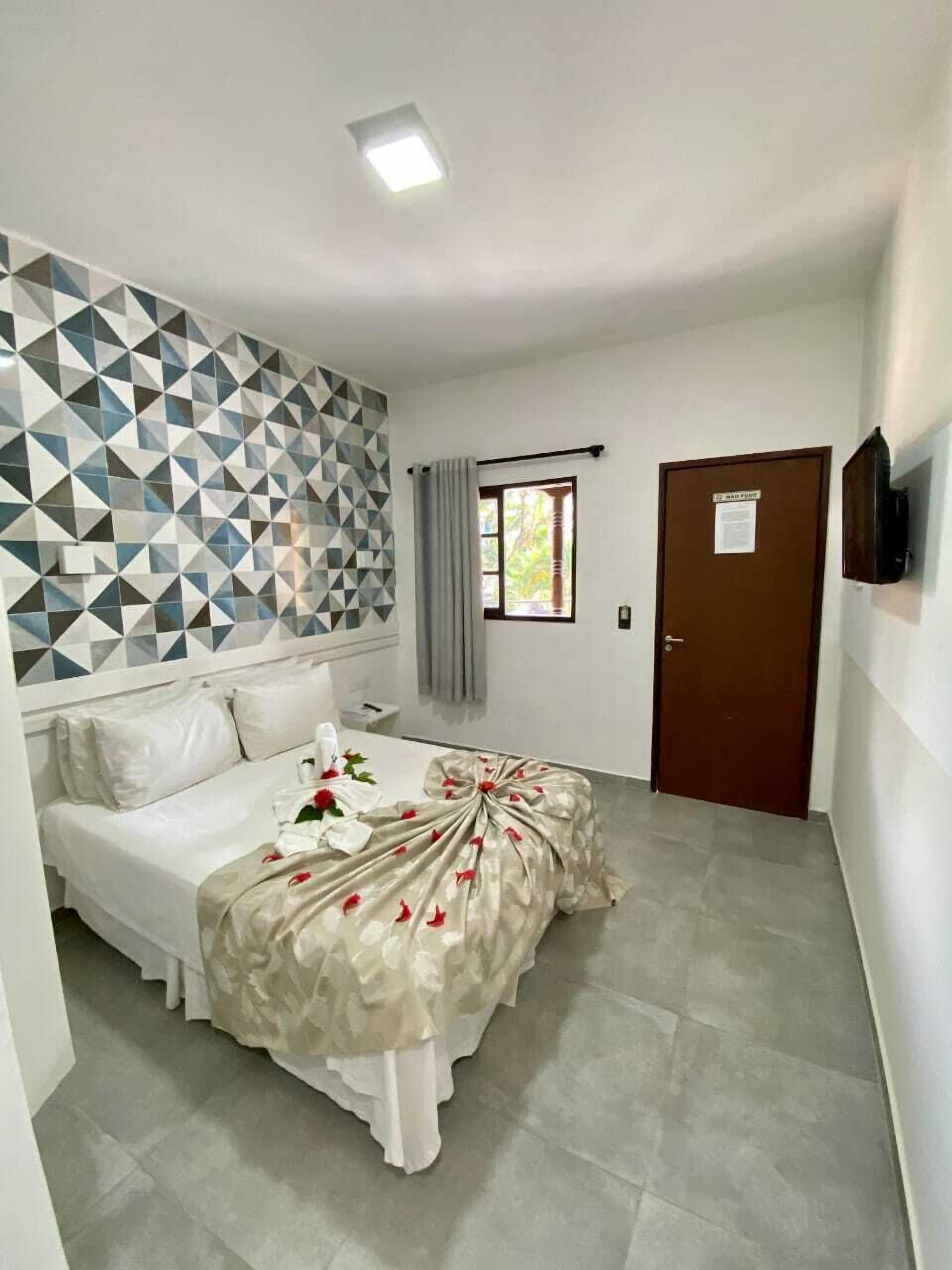 Une chambre d’hôtel avec un lit, un mur orné d’un motif géométrique, une fenêtre avec des rideaux, une porte et un téléviseur fixé au mur.