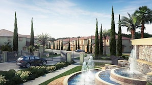 Un área residencial cerrada con una fuente, altos cipreses y una hilera de casas con techos de tejas rojas.