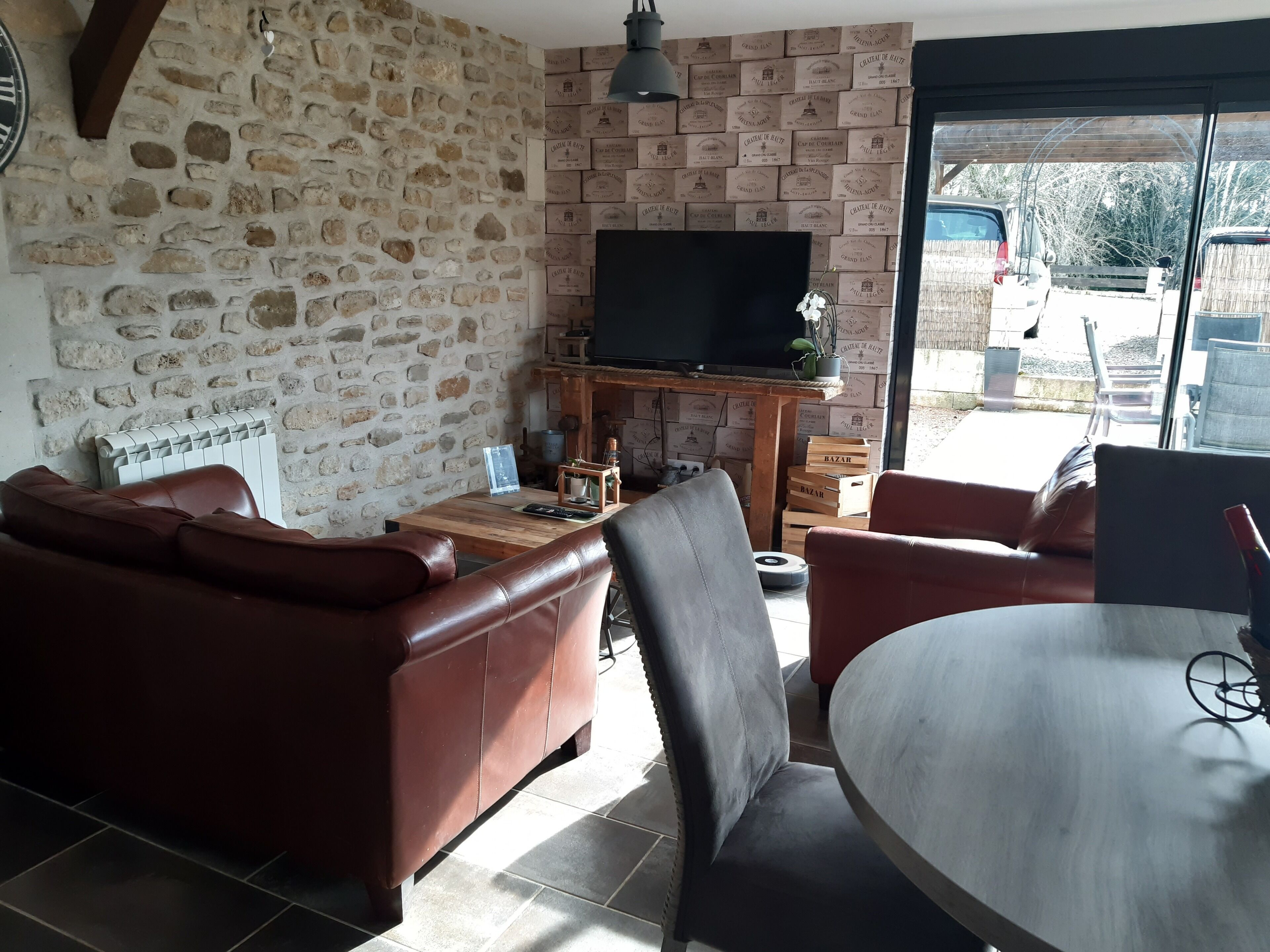 Un salon avec un mur en pierre, un canapé en cuir, une table basse en bois et un téléviseur posé sur un meuble.