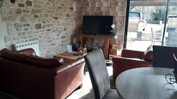 Un salon avec un mur en pierre, un canapé en cuir, une table basse en bois et un téléviseur posé sur un meuble.