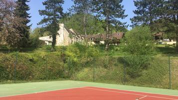 A tennis court with a green and red surface, surrounded by dense greenery and tall trees.