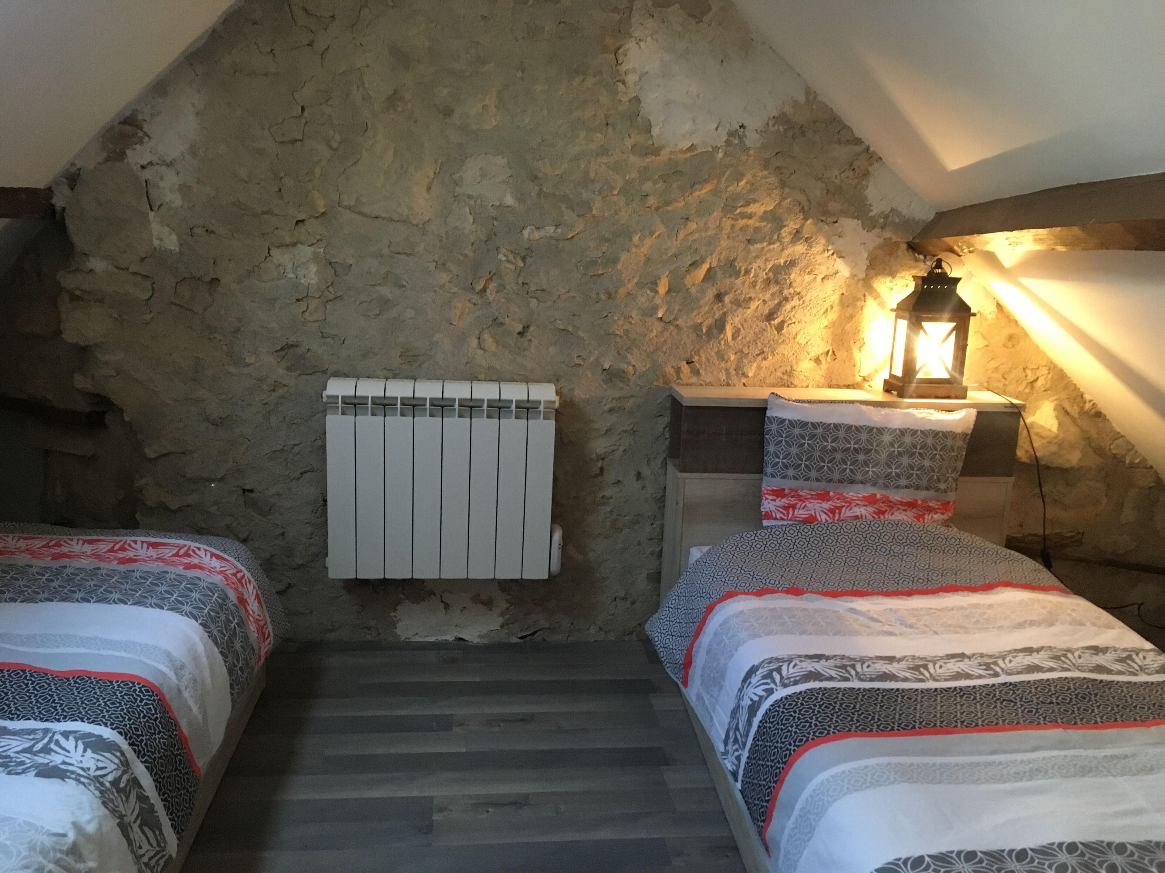 A cozy attic bedroom with two beds, a radiator, and a lantern providing light.