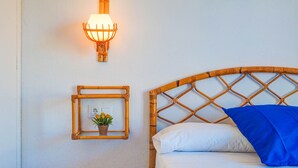 A bed with a woven headboard, a wall-mounted light fixture, and a small framed picture with a plant. - Aquamarine Terrace Apartment by Hello Homes Sitges (Sitges)