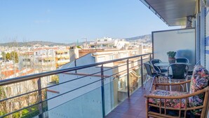 A balcony with a glass railing, wicker furniture, and a view of a cityscape. - Aquamarine Terrace Apartment by Hello Homes Sitges (Sitges)