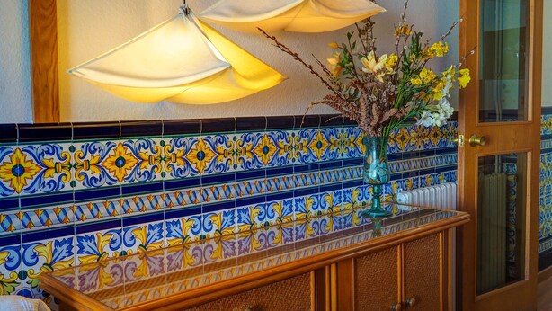 A tiled backsplash with a floral pattern, a wooden cabinet with a glass door, and a vase with flowers. - Aquamarine Terrace Apartment by Hello Homes Sitges (Sitges)
