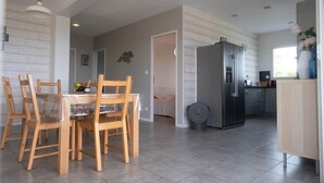 A modern kitchen with a refrigerator, a dining area with wooden chairs and a table, and a hallway leading to a bedroom. - Ardèche Home - Gite le Nid - Comfortable house with swimming pool, rated 4*. (Tauriers)