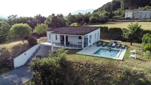 A modern house with a swimming pool, a covered patio, and a staircase leading to the entrance.