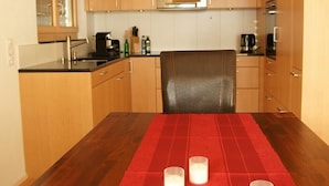 Een compacte keuken met houten kastjes, een magnetron en een eettafel met een rode tafelkleed en kaarsen.