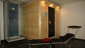 Een sauna met een glazen douchezijde, een houten sauna en een massagetafel met handdoek.