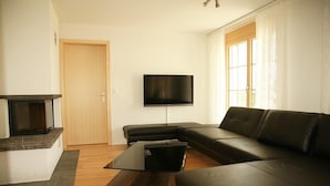 Een moderne woonkamer met een hoekbank, een flatscreen televisie aan de muur, een open haard en een houten salontafel.