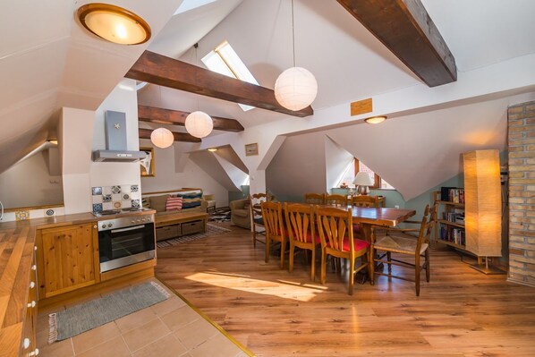 A spacious attic room with a kitchen, dining area, and bookshelves.