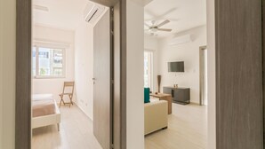 A spacious living area with a sofa, a small table, and a TV. There is a door leading to another room with a bed and a chair. - Paseo Del Mar B2B_200Mbps_Pool_Walk to Beach & Dining! (Bavaro-Punta Cana)