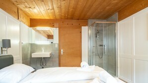 A hotel room with a wooden ceiling, a bed with white linens, a bathroom with a sink and shower, and a mirror.