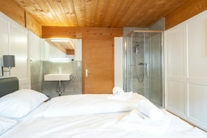 A hotel room with a wooden ceiling, a bed with white linens, a bathroom with a sink and shower, and a mirror.
