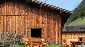 A rustic wooden barn with a large open door, a metal chair, and a fire pit in the foreground.