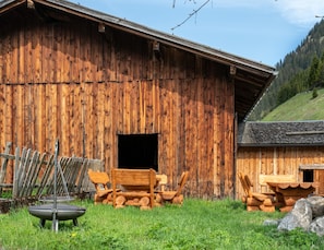 A rustic wooden barn with a large open door, a metal chair, and a fire pit in the foreground.