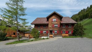 A two-story wooden building with a red-tiled roof, a sign reading 'Wiesenhof,' and a gravel driveway.