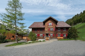 A two-story wooden building with a red-tiled roof, a sign reading 'Wiesenhof,' and a gravel driveway.