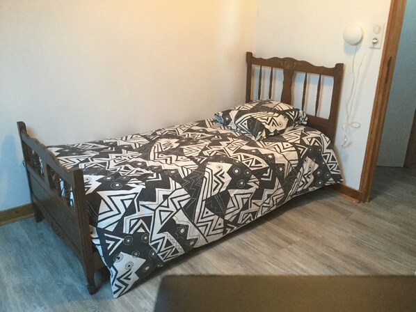 Una habitación pequeña con cama individual, un edredón estampado y un cabecero de madera.