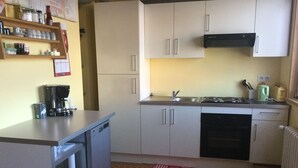 A compact kitchen with white cabinets, a built-in dishwasher, a coffee maker, and a kettle on the counter. - Cozy house in the countryside (Bolandoz)