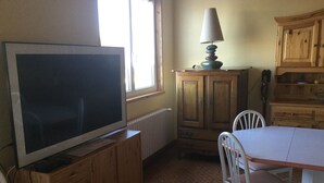 A compact kitchen with a television on a wooden cabinet, a table with chairs, and a window providing natural light. - Cozy house in the countryside (Bolandoz)