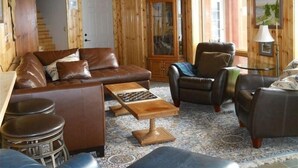 L’intérieur d’un chalet confortable, avec des murs en bois, un canapé en cuir marron, une table basse en bois et un fauteuil en cuir.
